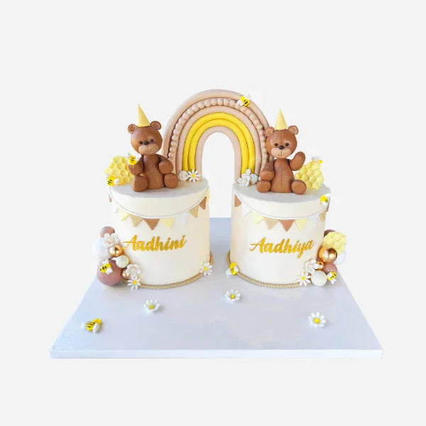 Two small cylindrical cakes with teddy bears and a rainbow on top, on a white background.